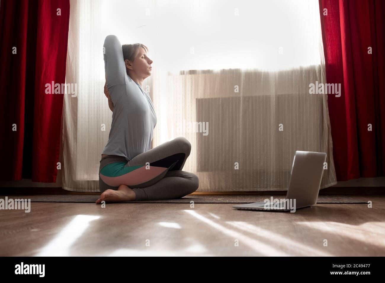 Woman in sitting yoga pose cow face asana during online lesson on laptop. Stock Photo