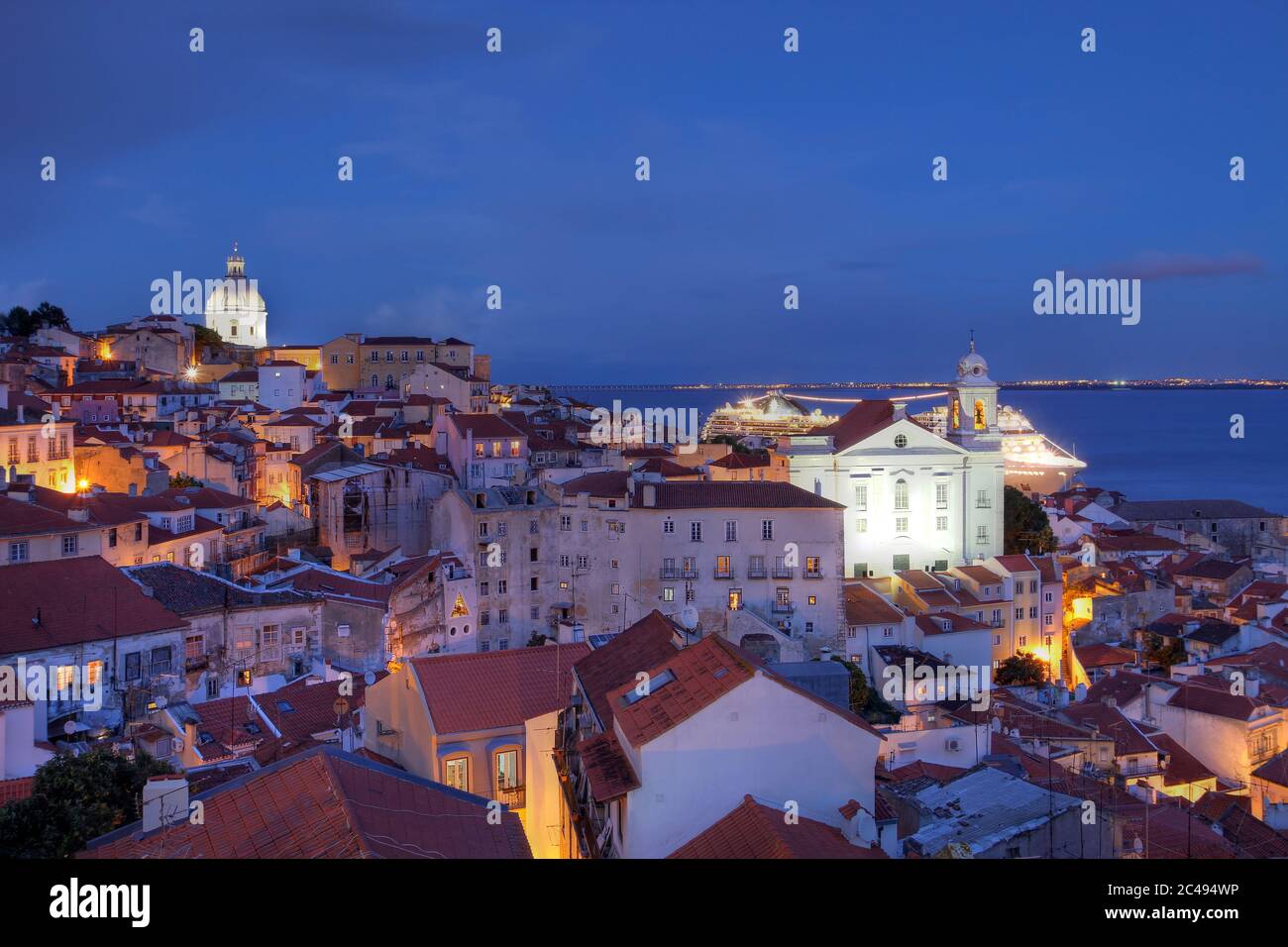 Twilight view over Alfama (ancient quarter of Lisbon, Portugal) as seen from the Miradouro (Belvedere) de Santa Lucia with St-Stephen Church Stock Photo