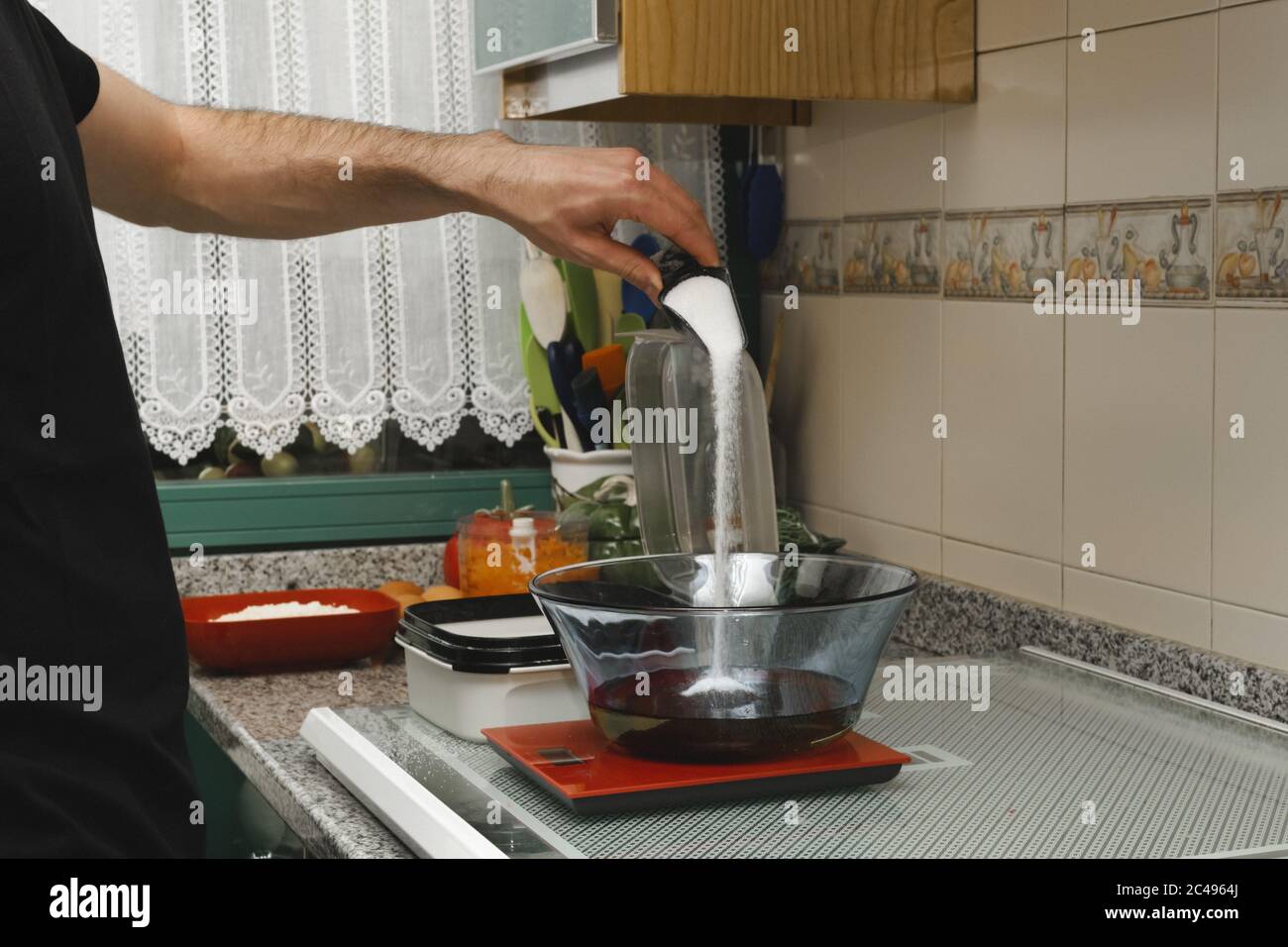 Man pouring sugar in a glass bowl that's on the weighing scale in the ...