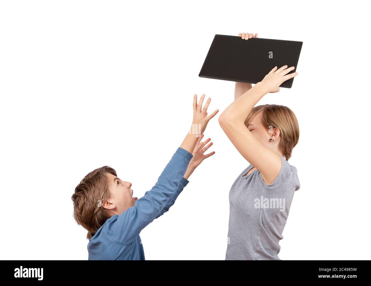 Siblings fighting for the laptop. The broher wants  the notebook, his sister holding it above her head.. Studio shot isolated on white. Stock Photo