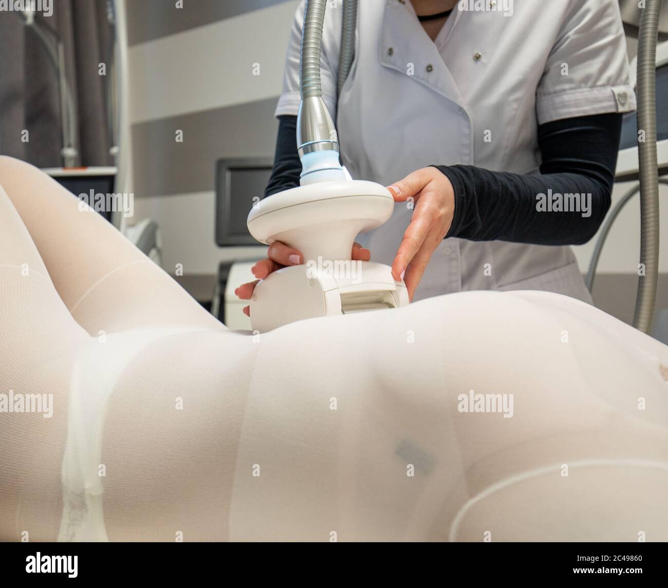 Woman in white suit having anti cellulite treatment with therapist in cosmetology clinic. Lipo massage apparatus procedure on womans stomach Stock Photo