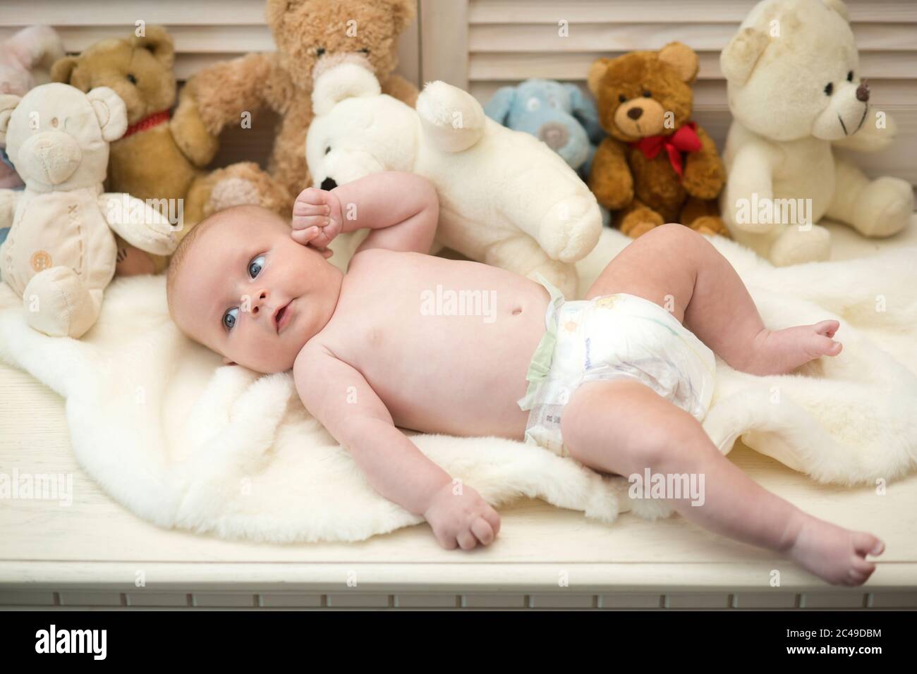 Baby lying on white duvet. Infant with blue eyes and curious face ...