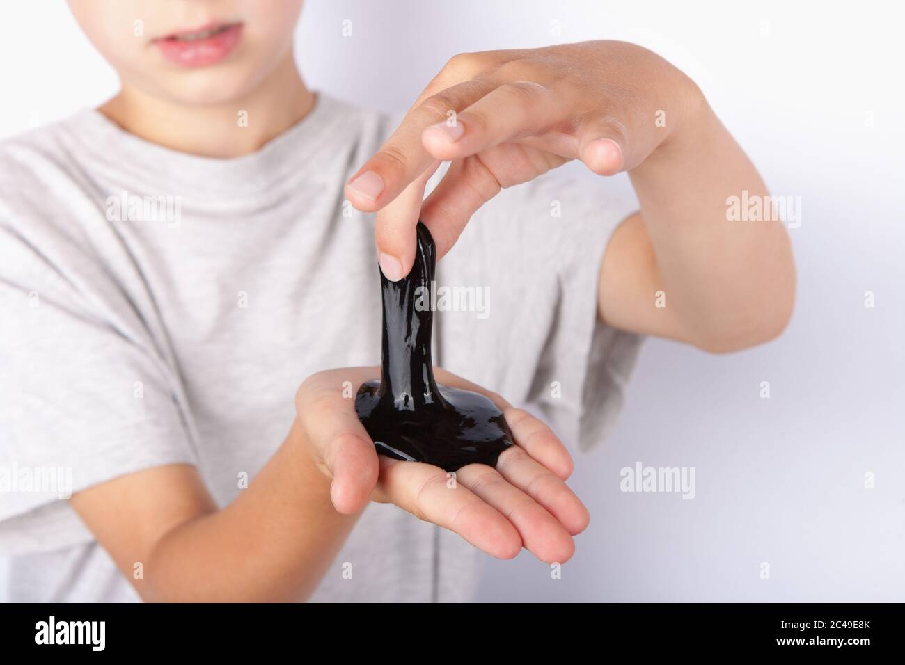 Young boy holding a black slime toy on his palm and formatting it with his another hand Stock Photo