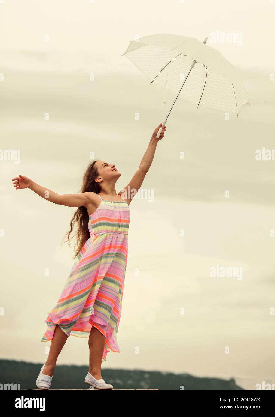 Feeling light. Anti gravitation. Fly drop parachute. Dreaming about first flight. Kid pretending fly. I believe i can fly. Touch sky. Girl with light umbrella. Fairy tale character. Happy childhood. Stock Photo