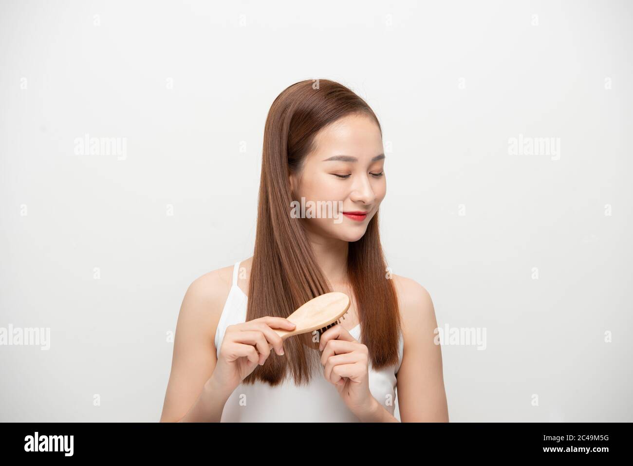 Beautiful young Asian woman combing her hair over background. Stock Photo