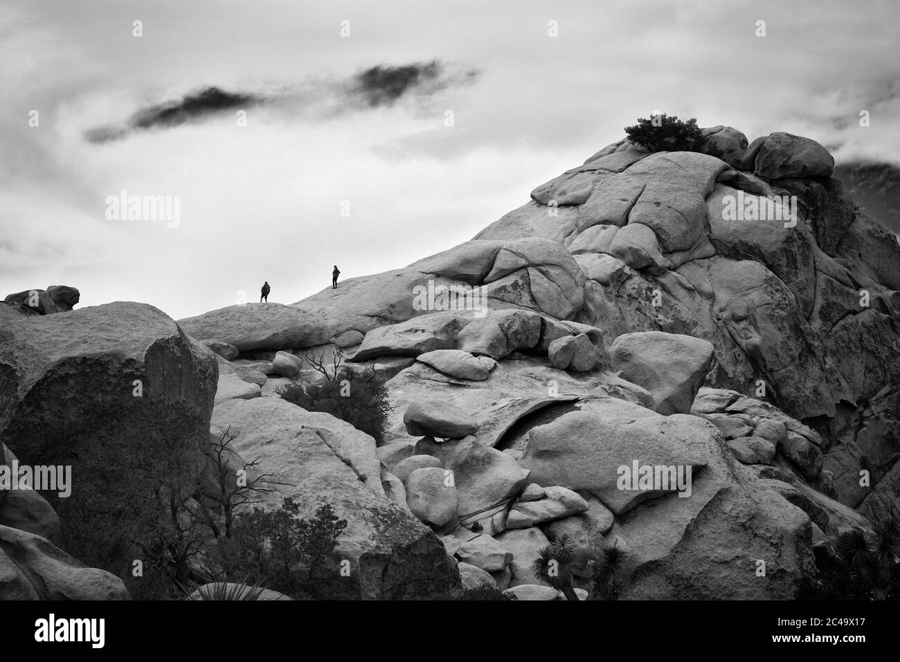 Two people climbed up a rocky hill during a hike. The clouds in the sky announce some rain within the desert. Stock Photo