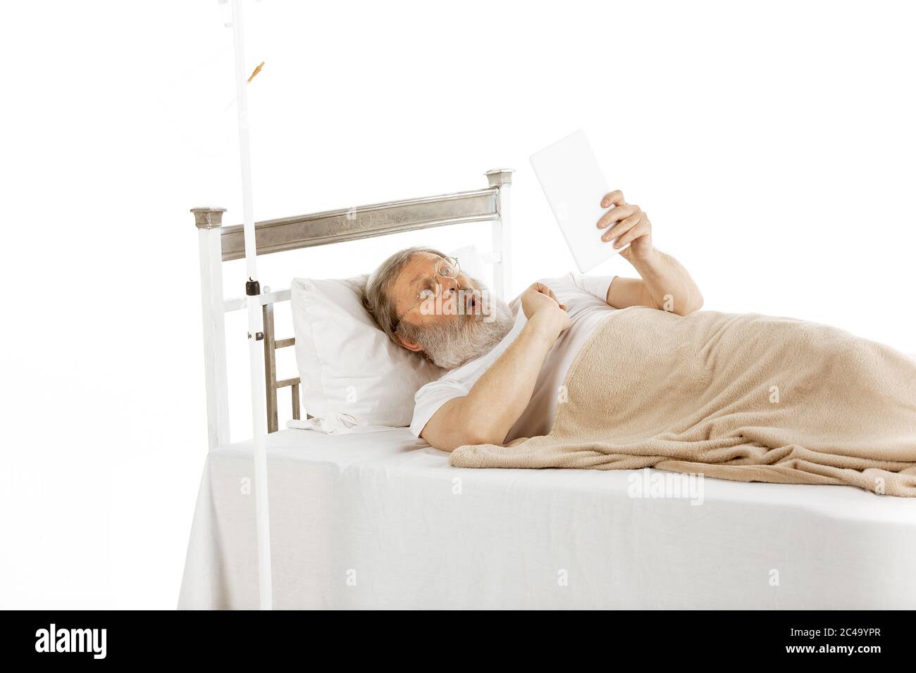 Elderly old man recovering in a comfortable hospital bed isolated on white  background. Getting treatment and care. Concept of healthcare and medicine.  Lying, scrolling tablet, shocked. Copyspace Stock Photo - Alamy
