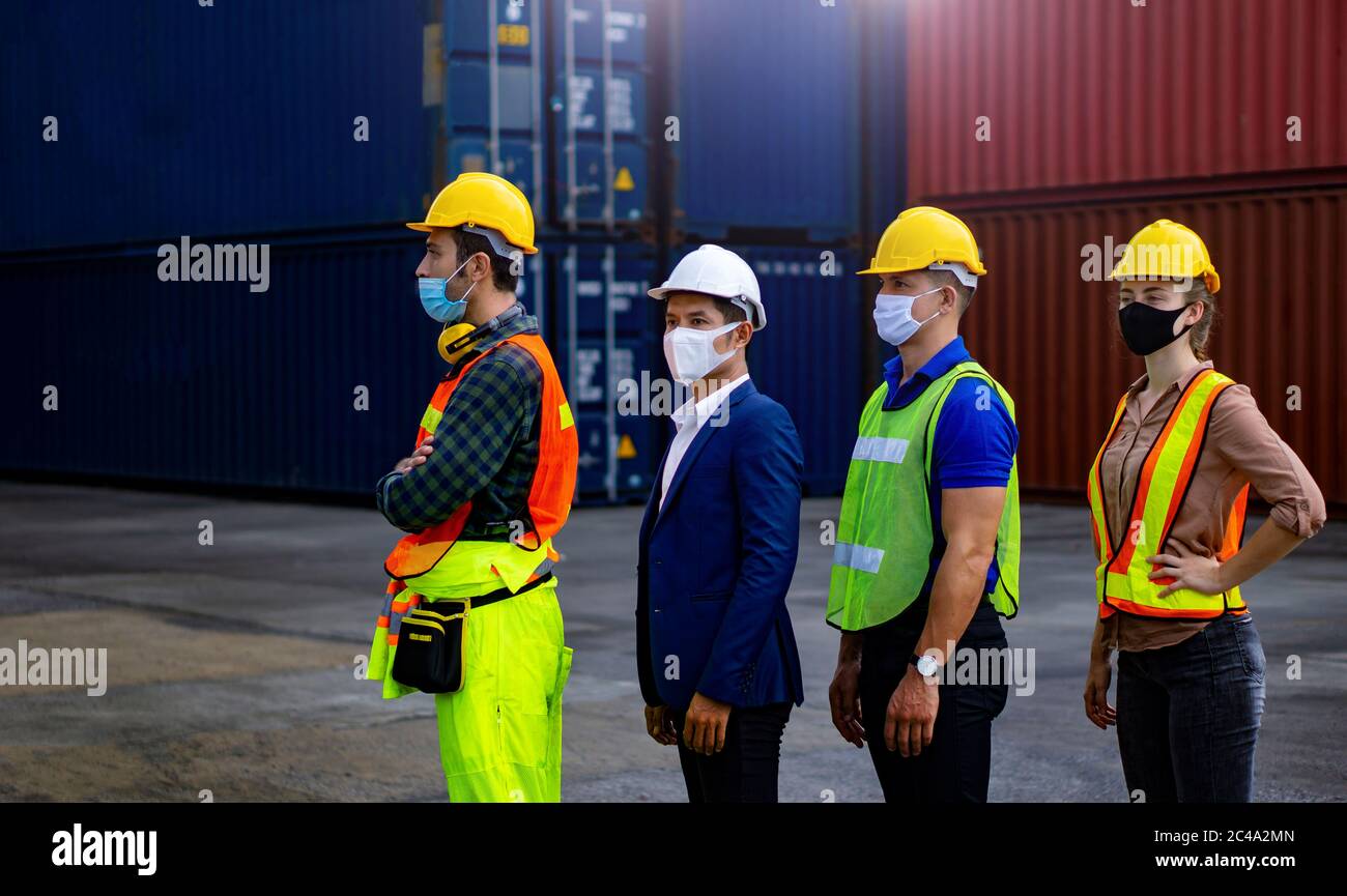Industrial workers or engineers wearing Coronavirus or COVID-19 protective masks stand in front of the shipping container. Stock Photo