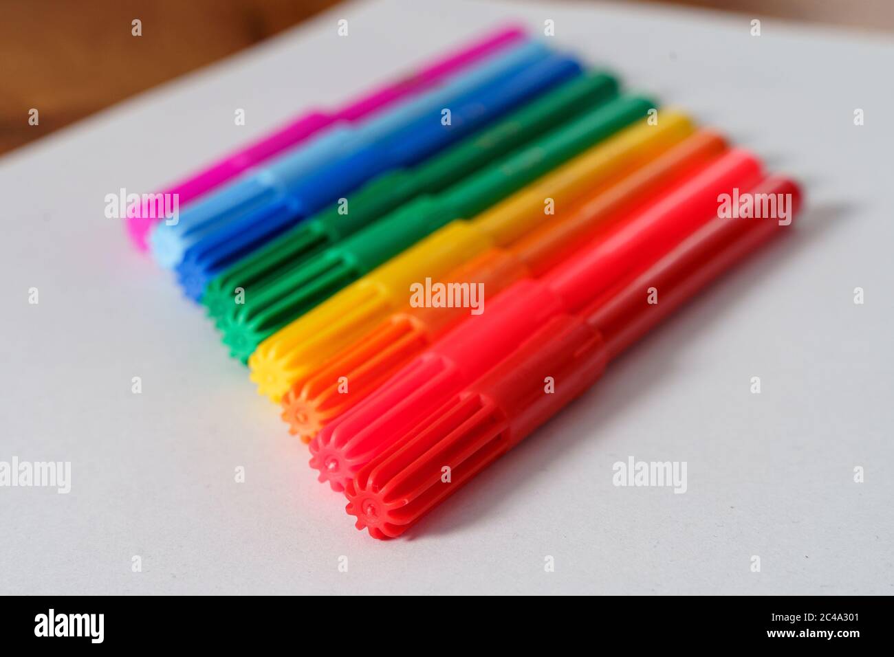 Colored markers on a white sheet and brown table. Stock Photo