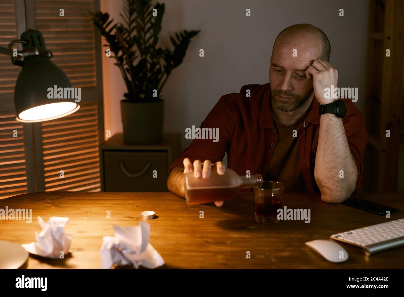 Mature man sitting at the table in depression and pouring whiskey into the glass he is in depression Stock Photo