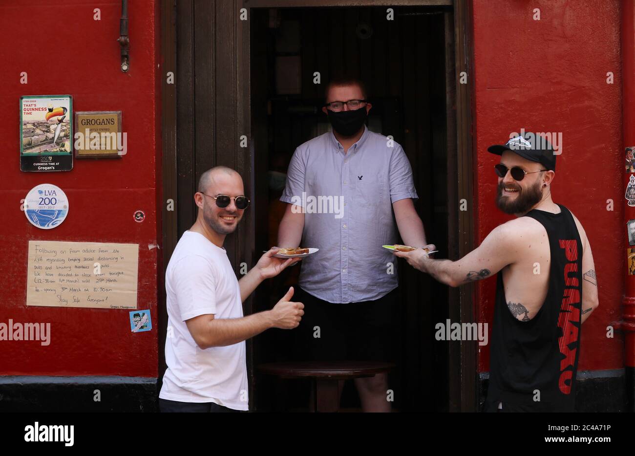 Harry Lewis (left) and Sean Watmore (right) receive their free toasted sandwiches from barman Daniel Smith at Grogans Castle Lounge in Dublin's city centre. The pub announced on social media that they would be handing out some of their much loved toasties for free this afternoon. Pubs and hotel bars operating as restaurants can begin to reopen to the public on Monday 29th June in line with the Government's Phase 3 of easing of COVID-19 restrictions. Stock Photo