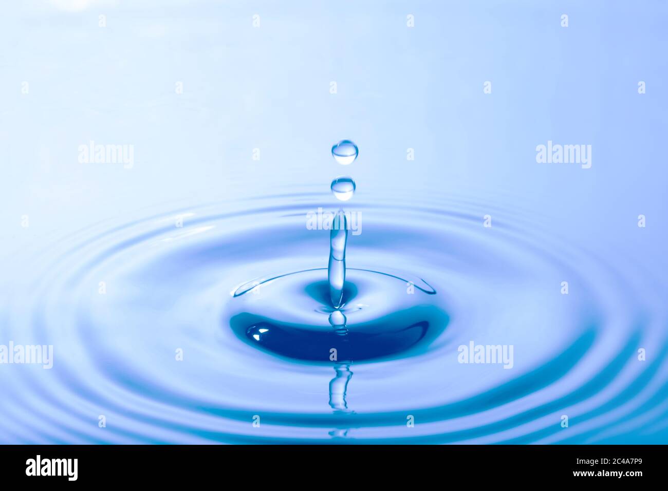 Water droplet falling impact with water surface. causing rings on water surface. Stock Photo