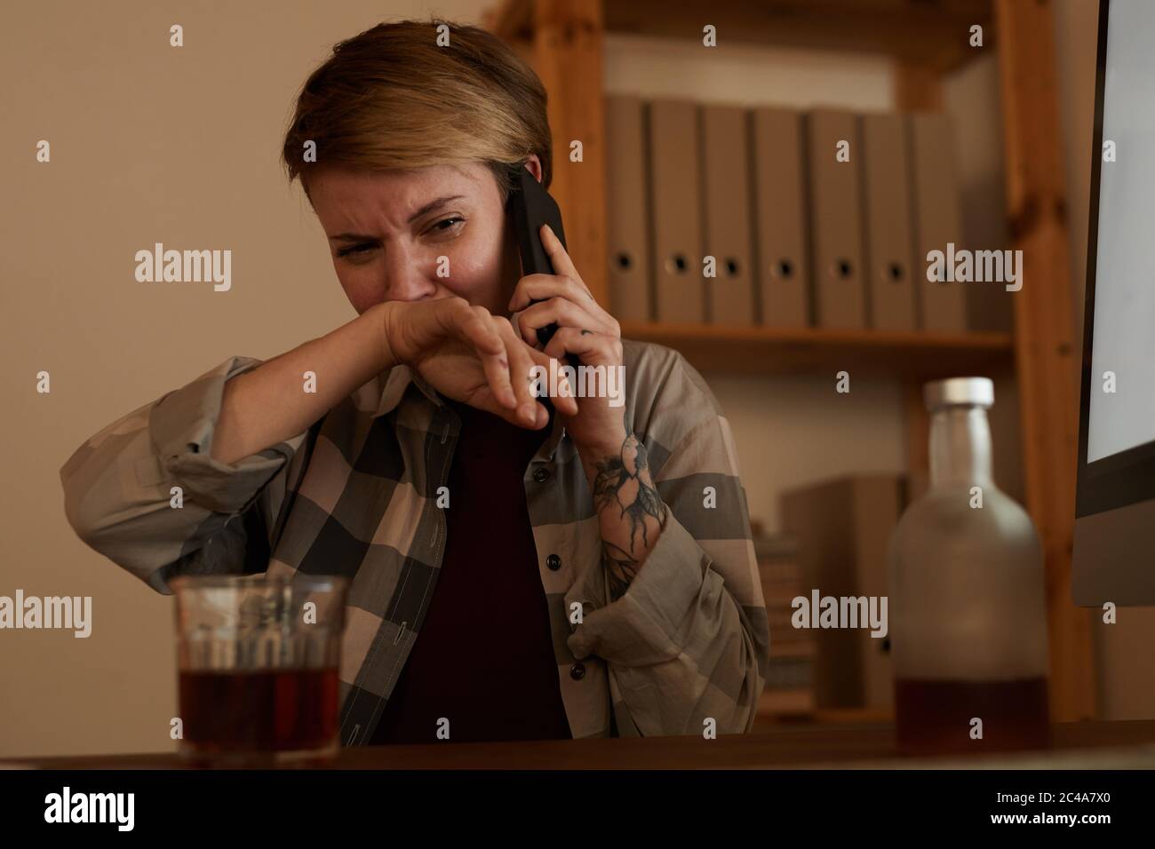 Young woman drinking alcohol and telling about her problems to somebody on mobile phone Stock Photo