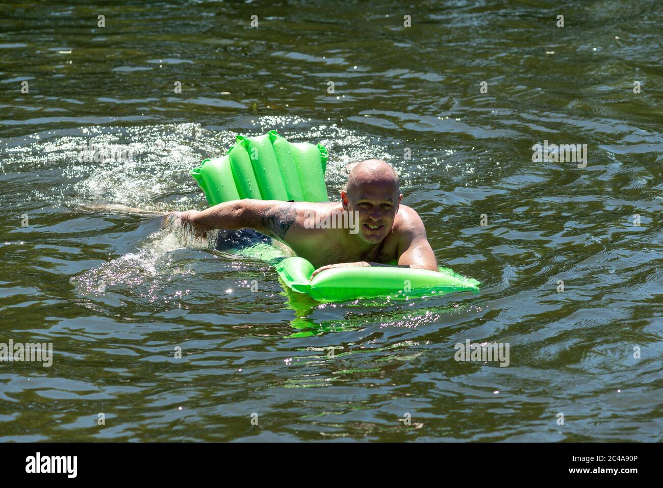 Man on a lilo swimming in the River Avon cooling off in the cold water. Mid-summer heatwave making it the hottest day with the highest UV levels so far this year and the temperature at around 33 degrees in the afternoon. Fordingbridge, New Forest, Hampshire, England, UK, 25th June 2020. Stock Photo
