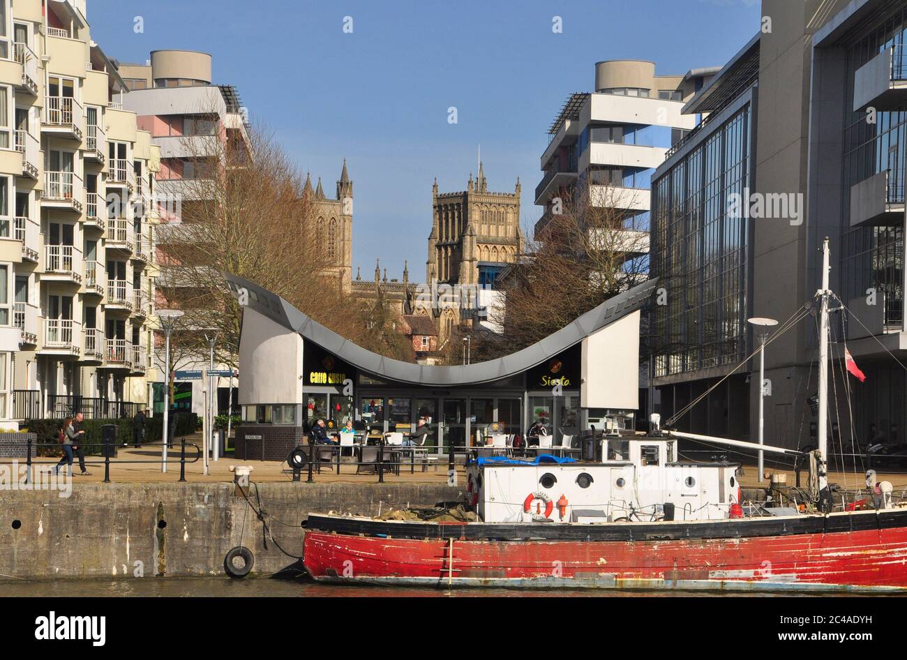 Bristol's Anglican Cathedral framed by the modern office and accomodation developments on the nearby harbour with an old wooden boat moored at the qua Stock Photo