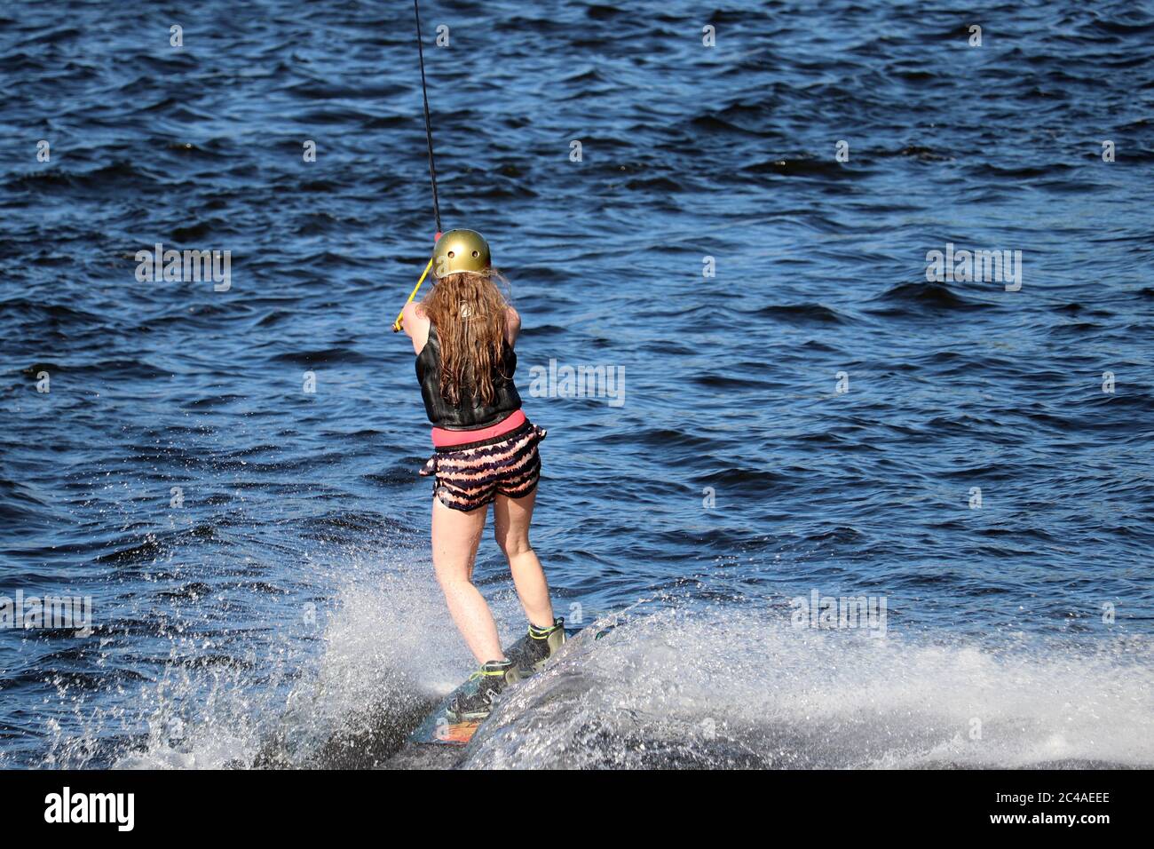 Wakeboarding in sunny day, girl riding on board in a spray of water. Surfer in the sea, summer sport Stock Photo