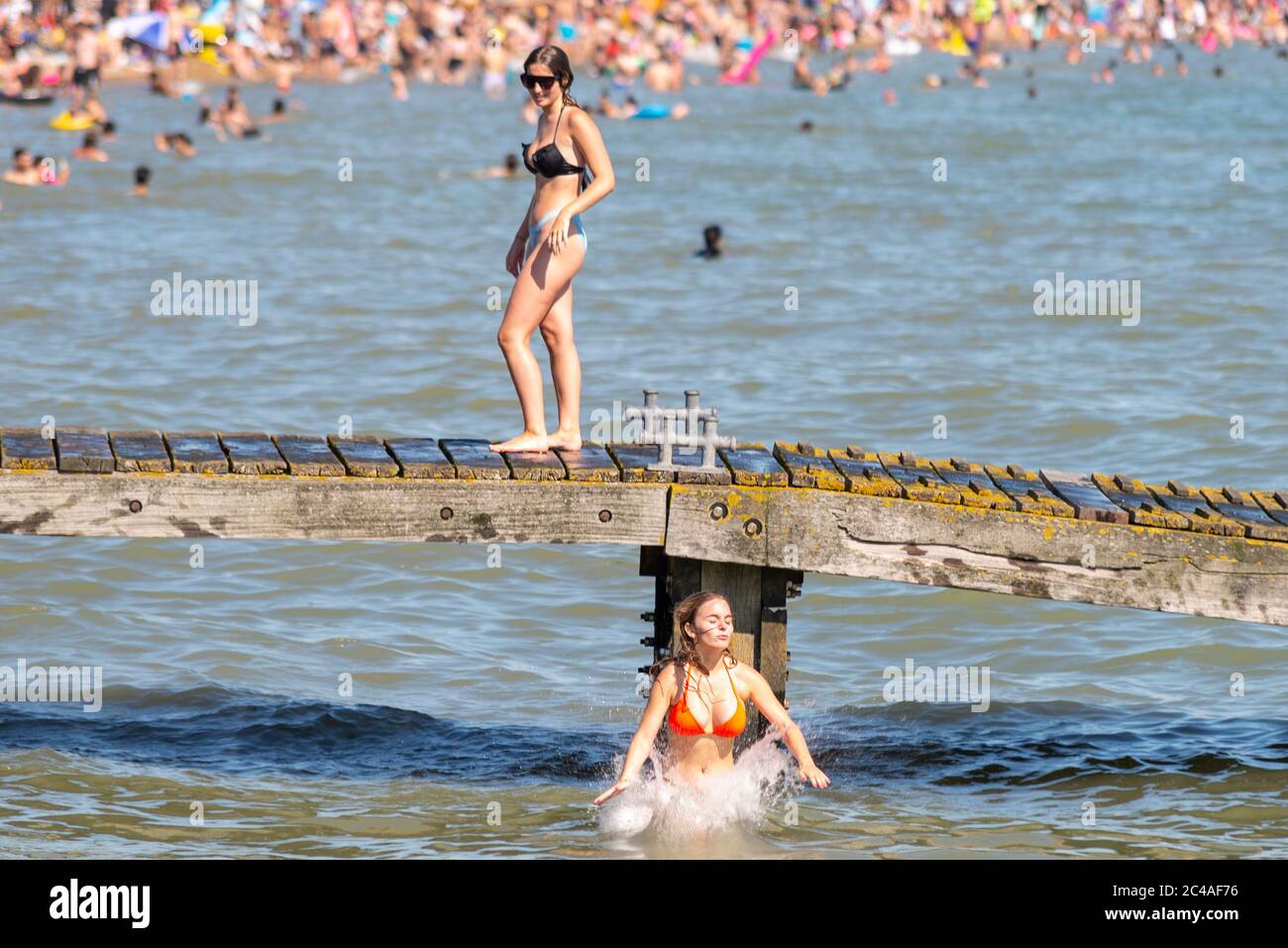 Southend on Sea, Essex, UK. 25th Jun, 2020. With the forecast record temperatures for 2020 people are heading to the seafront to cool down, despite the COVID-19 Coronavirus advice. In Southend on Sea the shore of the Thames Estuary is packed, with people swimming and jumping into the sea. Young white Caucasian female landing in the sea Stock Photo