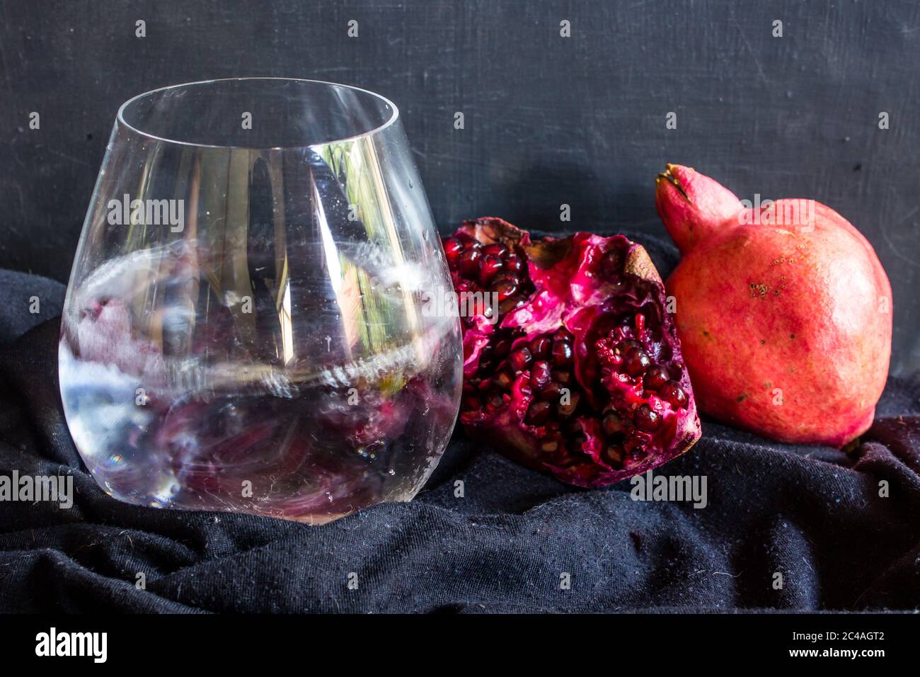 A gin and Tonic, garnished with large amount of Pomegranate pits, with pomegranates, on a black background Stock Photo
