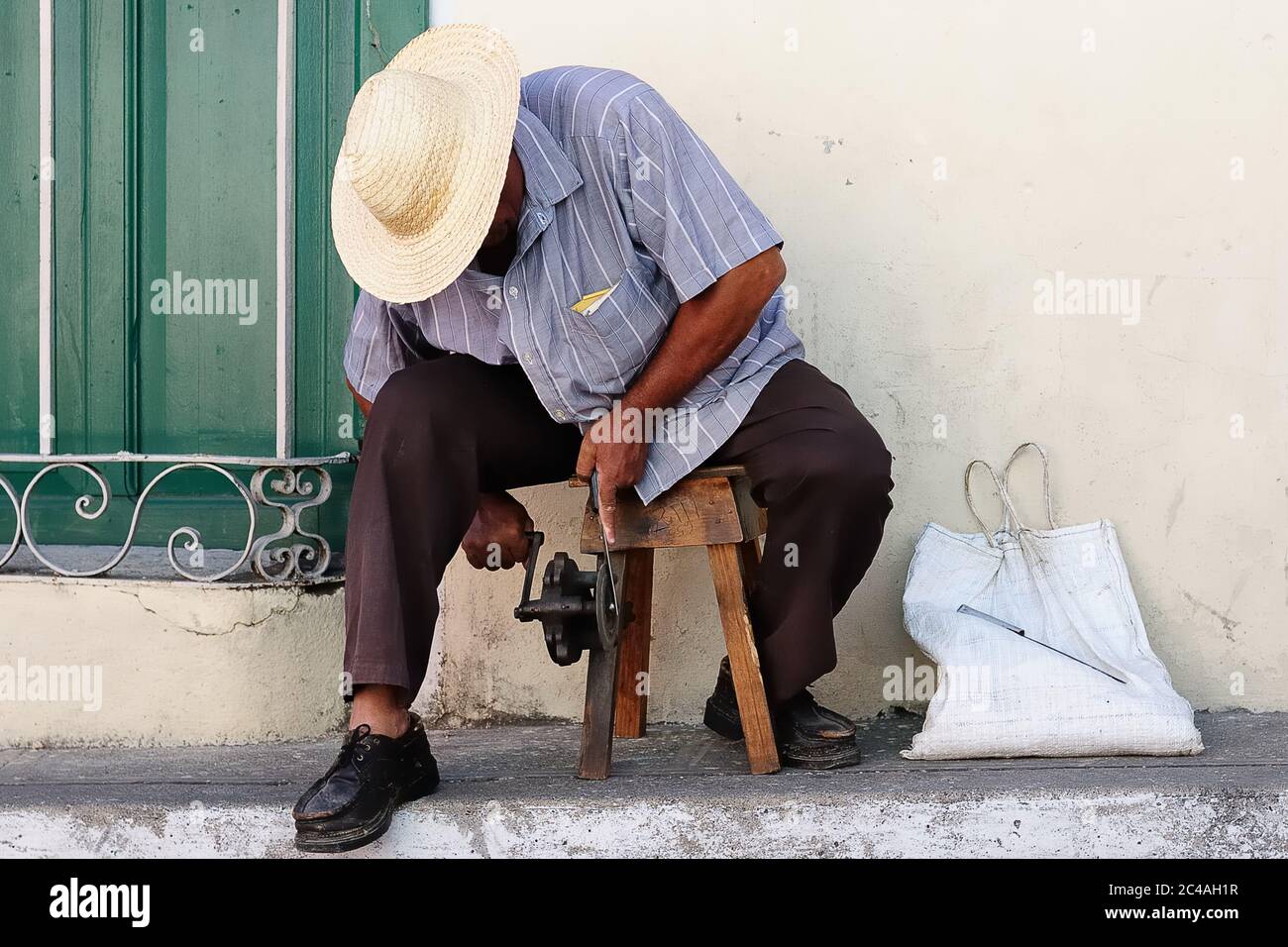 The photograph is showing the street life on Cuba, the man is sharpening knives on the pavement in Santiago de Cuba, Cuba Stock Photo