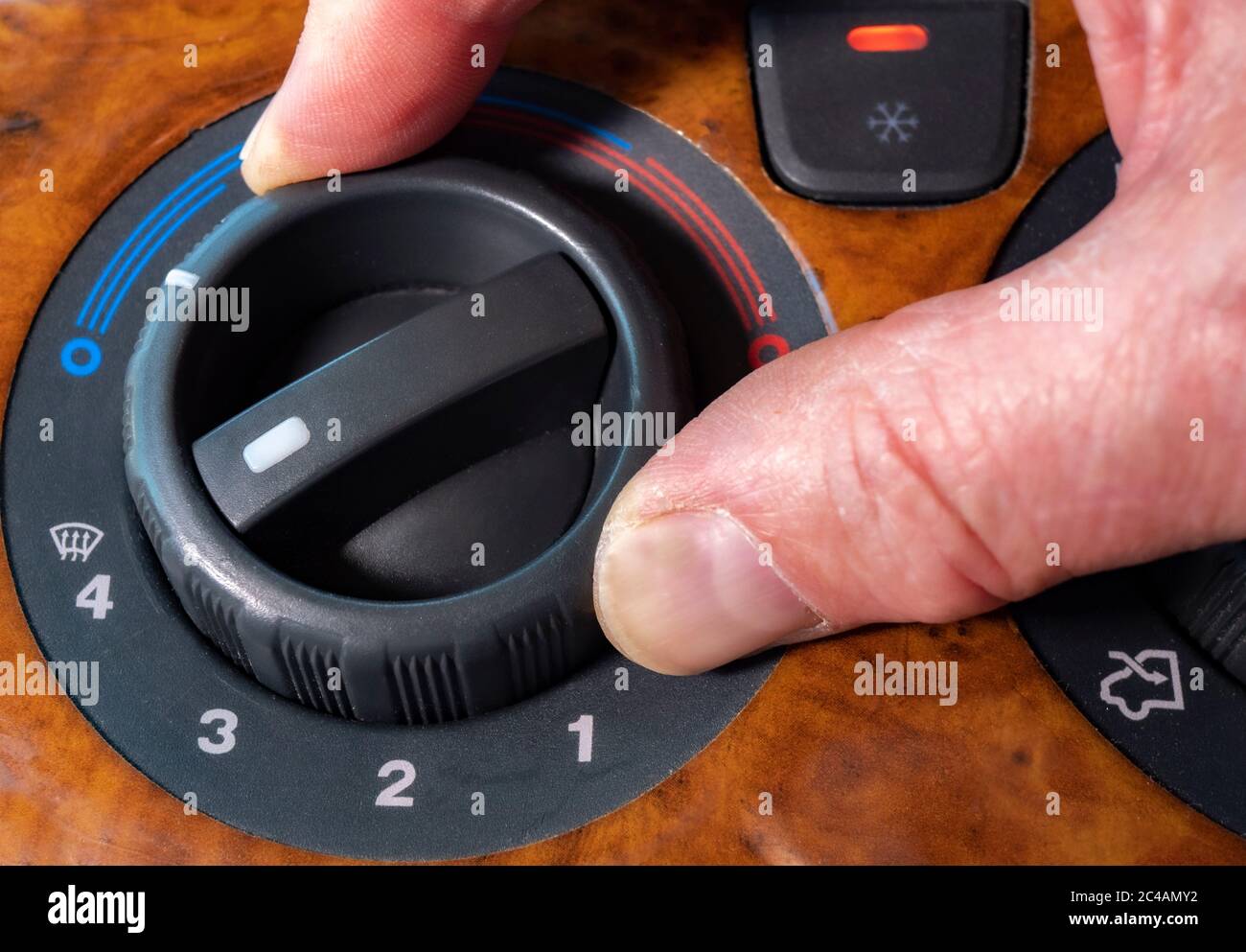 Finger and thumb turning vehicle air-conditioning dial, with light on and output turned to coldest (blue) and the strongest fan for maximum cooling. Stock Photo