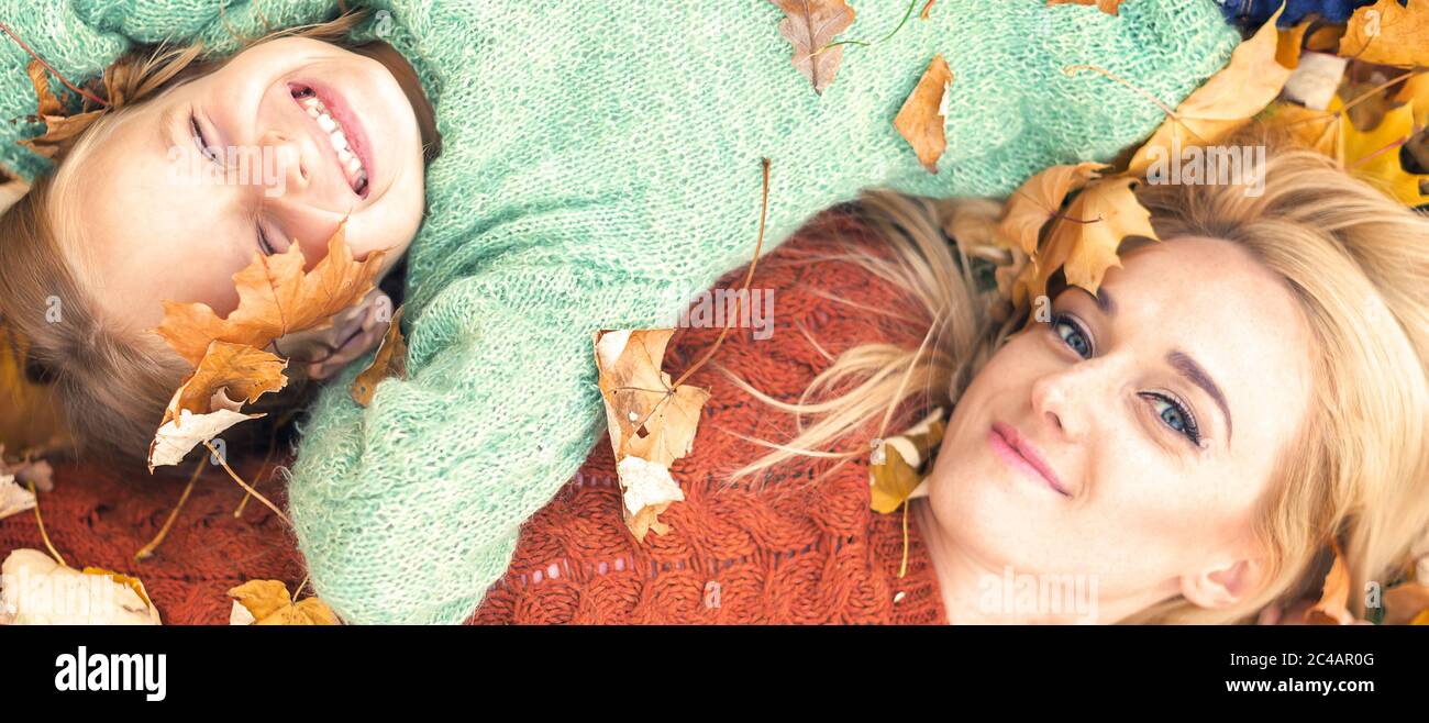 Little girl and young caucasian mom lying down directly above looking at camera on autumn leaves Stock Photo