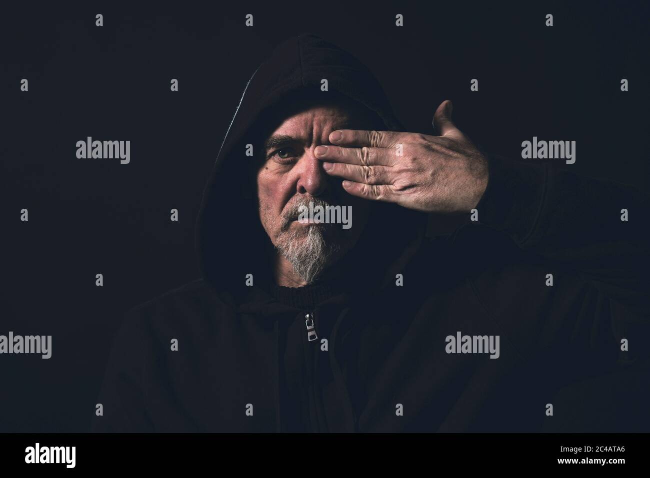 portrait of a man wearing a hoodie, holding one hand in front of an eye Stock Photo