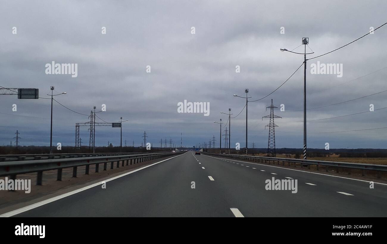 A road or a highway, the highway stretches to the horizon. View from the car window. Journey, the way home. Cold northern nature, summer, gray cloudy low sky. Stock Photo