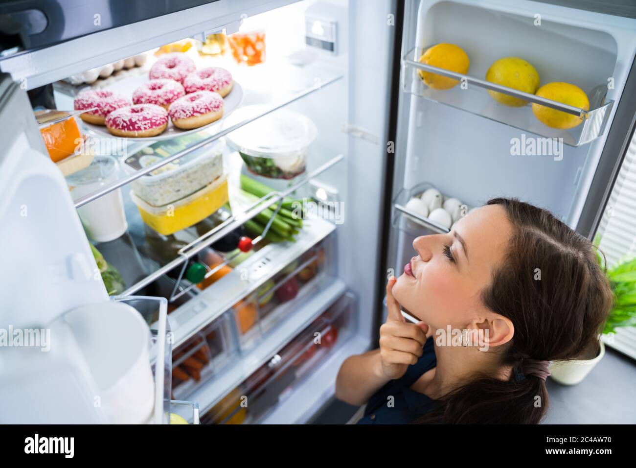 Hungry Woman Looking For Food In Kitchen At Home Stock Photo