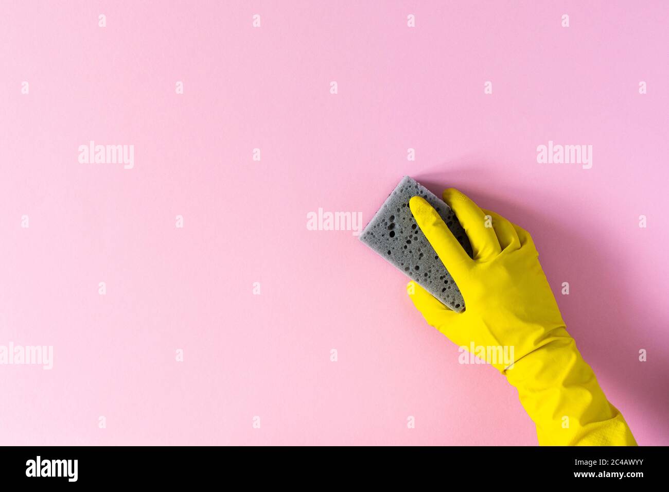 Hand in a yellow rubber glove with a cleaning sponge on a pink ...