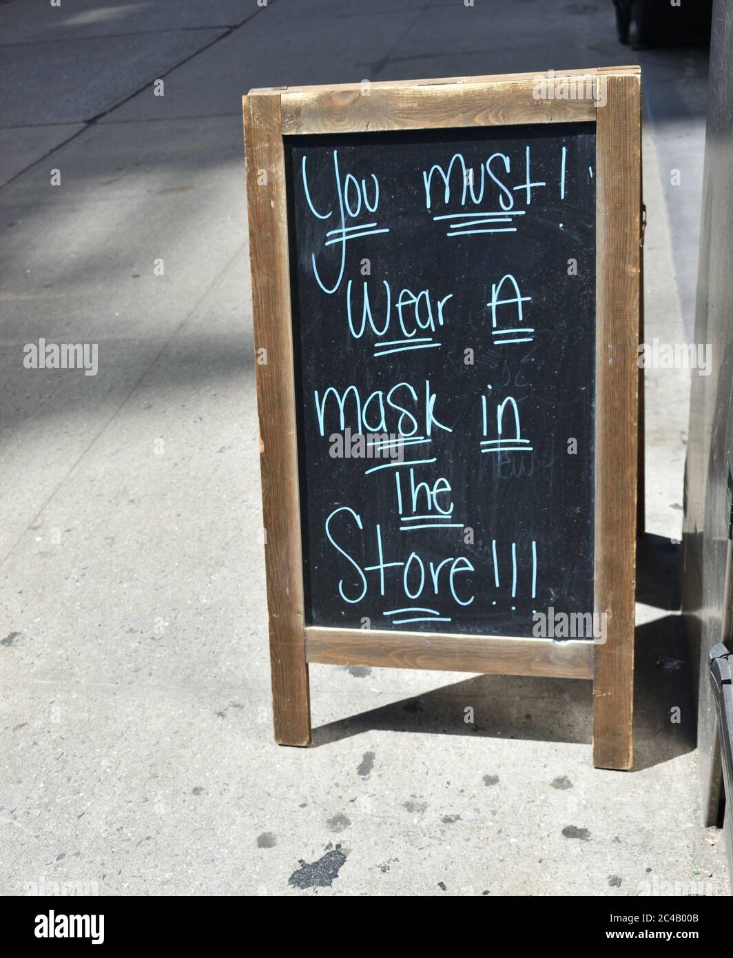 A-frame blackboard sign reading 'You must wear a mask in the store!!!' on a city sidewalk in front of a grocery store, May 22, 2020, in New York. Stock Photo