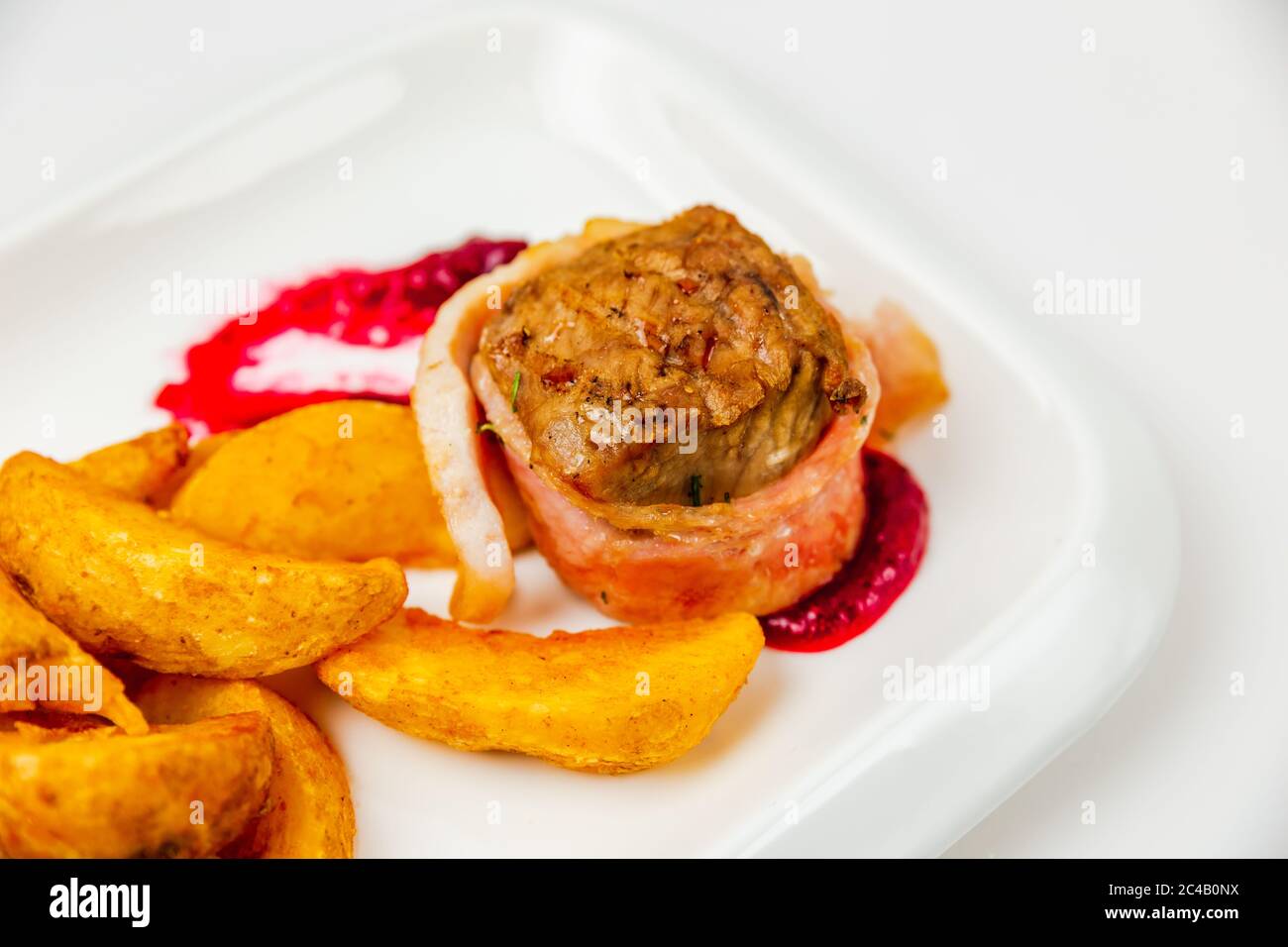 Fillet mignon rolled in bacon and baked in oven with berry sauce. Potato for garnish. Close-up photo Stock Photo