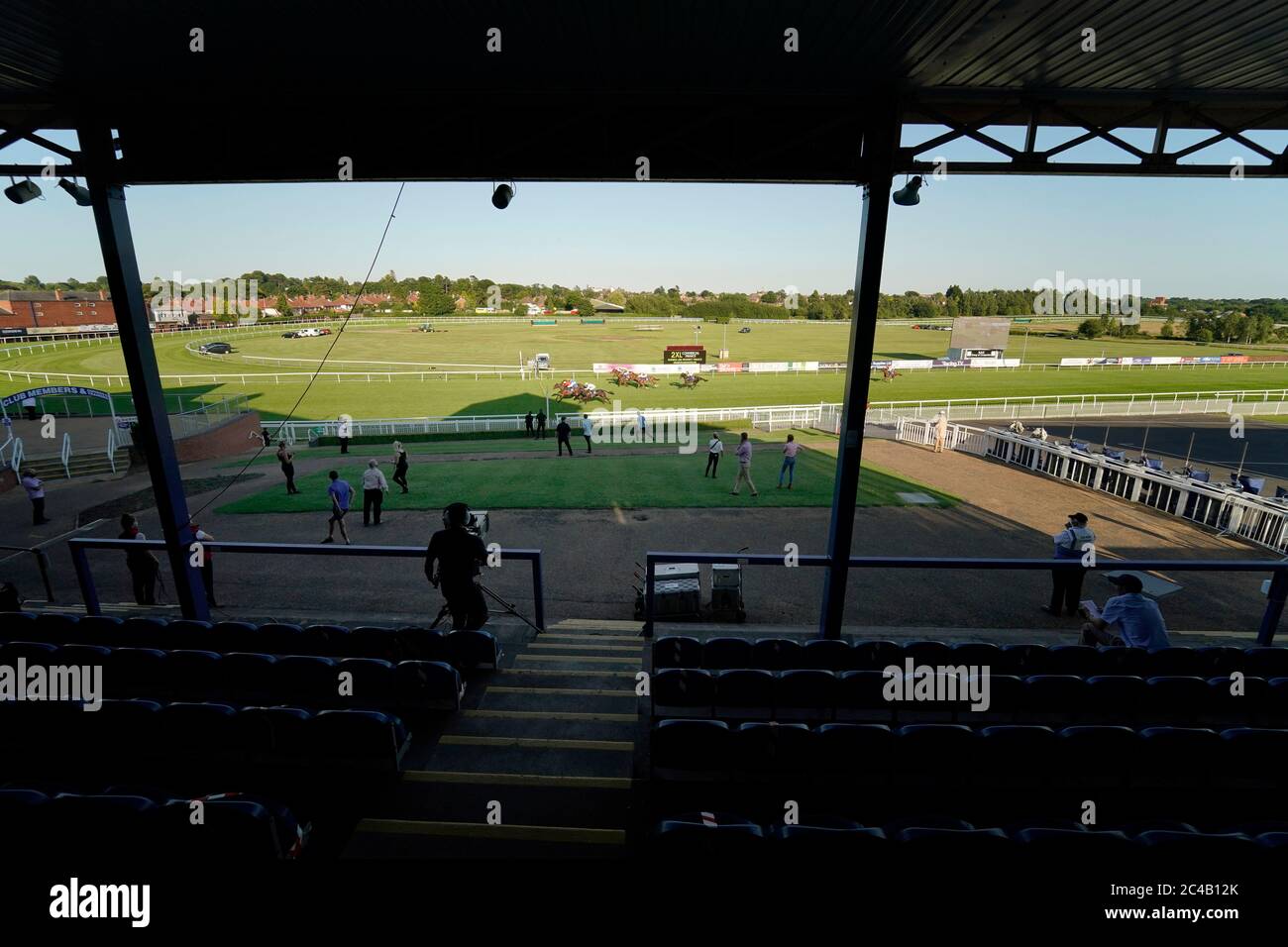 A general view as the stable lads and lasses watch the action from the grandstand lawn as Paddy Mathers riding Destroyer (red silks) wins The Larsen Building Products Handicap at Leicester Racecourse. Stock Photo