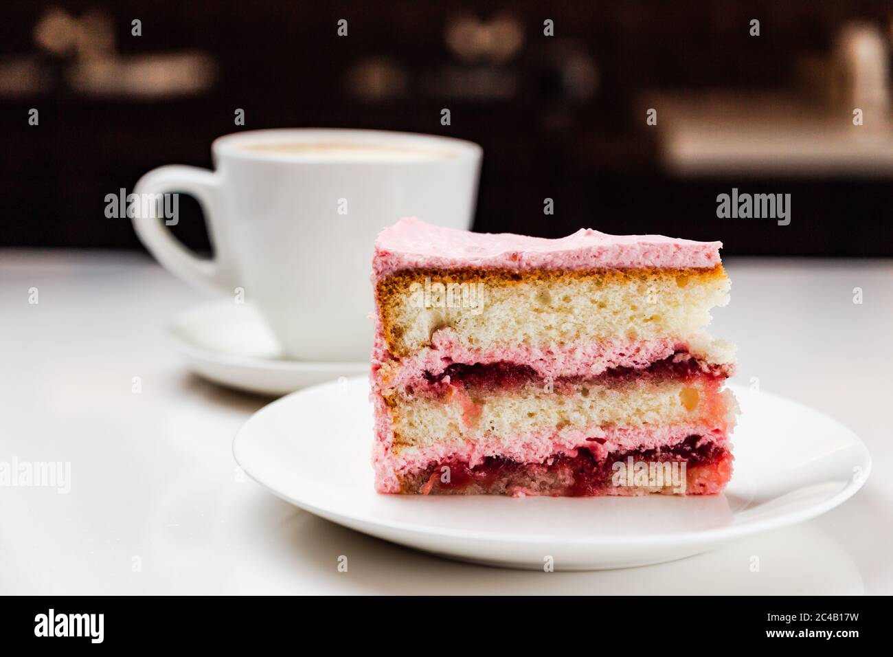 Strawberry yoghurt cake on a white plate and a cup of cappuccino coffee