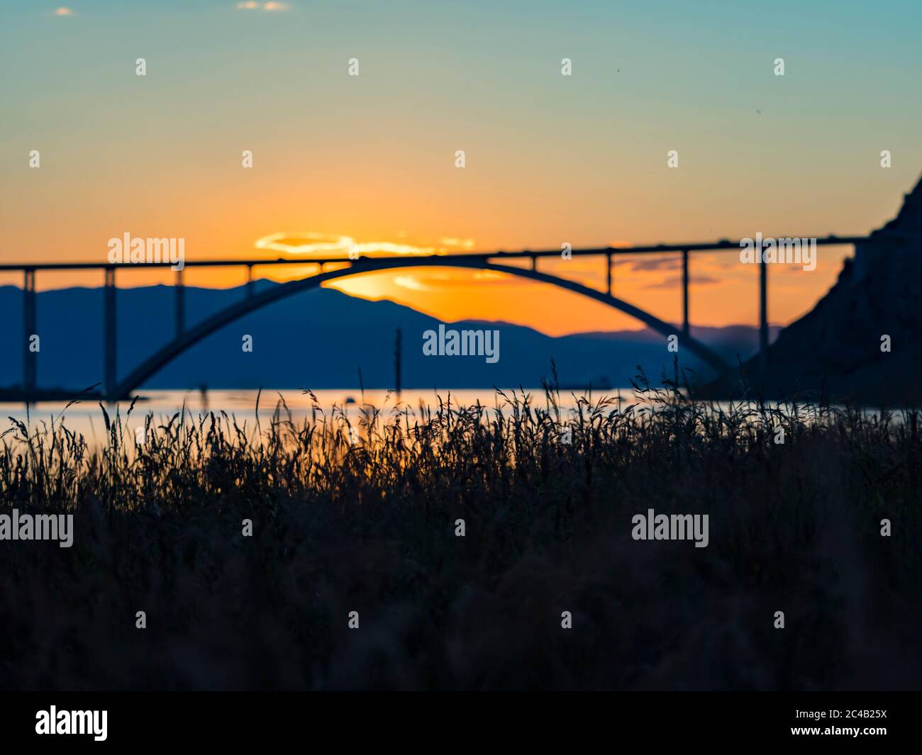 Sunset landscape silhouette silhouetting grass in foreground bridge mainland to island Krk Croatia Stock Photo