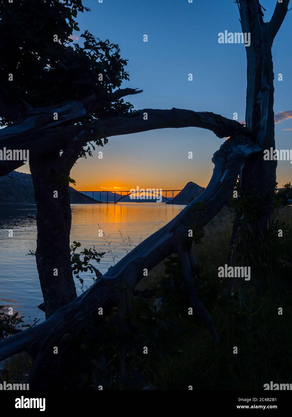 Sunset landscape silhouette silhouetting trees framed bridge mainland to island Krk Croatia Stock Photo