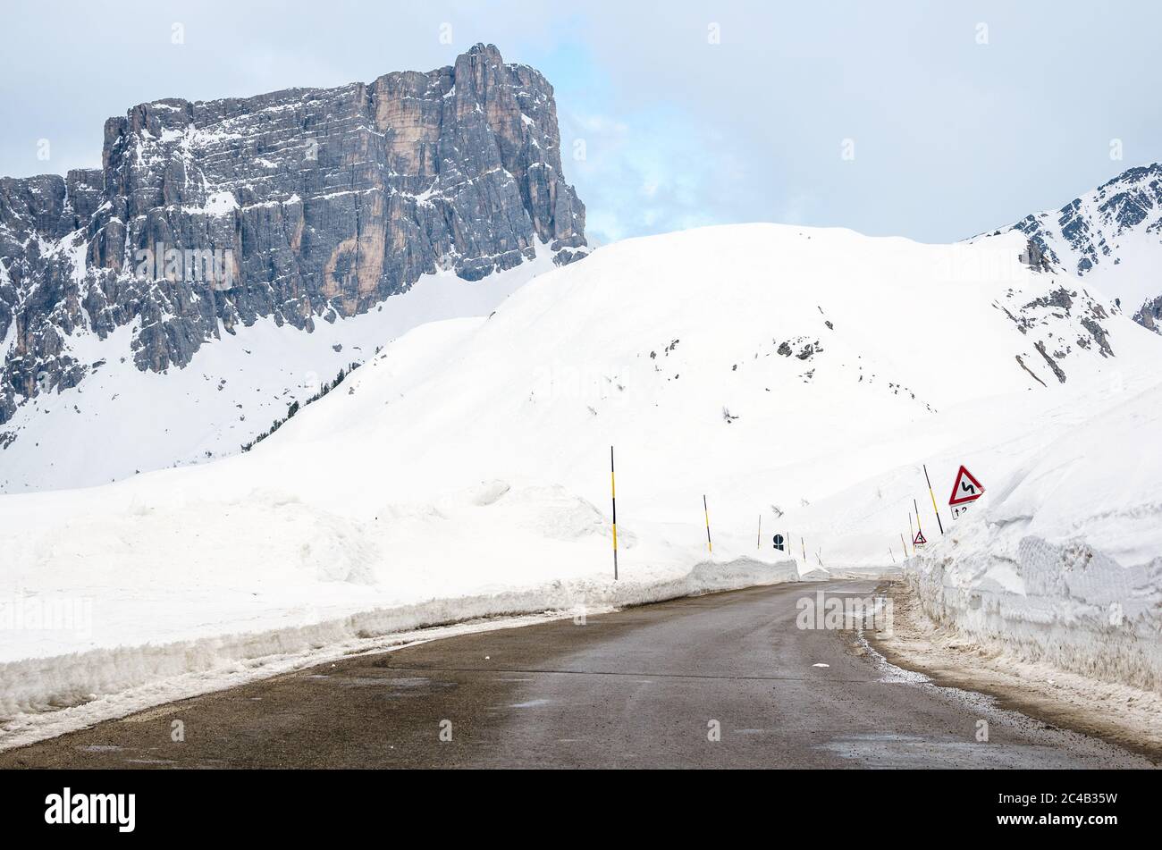 Deserted mountain pass road in the European Alps in winter. A towering rocky peak is visible in background. Stock Photo