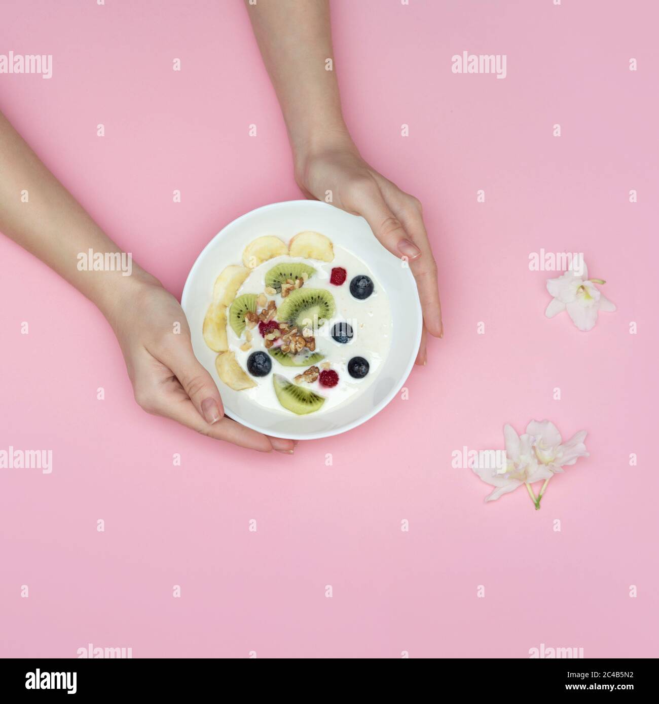 Female hands holding a bowl of smoothies with superfoods. Yogurt. blueberries, kiwi, almonds, banana, nuts. Top view on a pink background. Stock Photo
