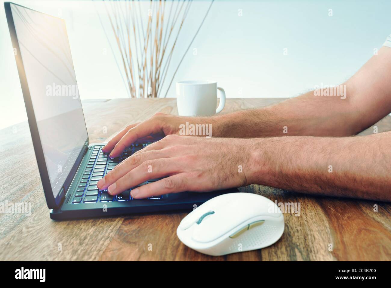 low angle view of man using laptop computer on wooden table with bright sunlight coming through window Stock Photo