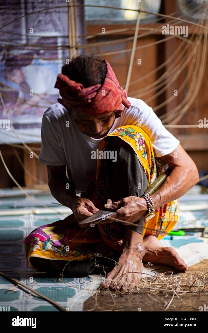 Malaysian kite maker working on a kite in his workshop in low light. Stock Photo