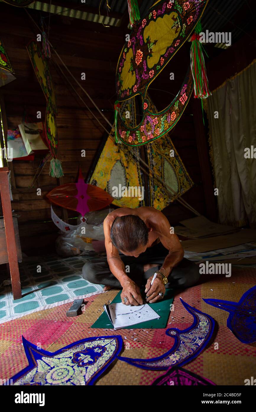 Malaysian kite maker working on a kite in his workshop in low light ...