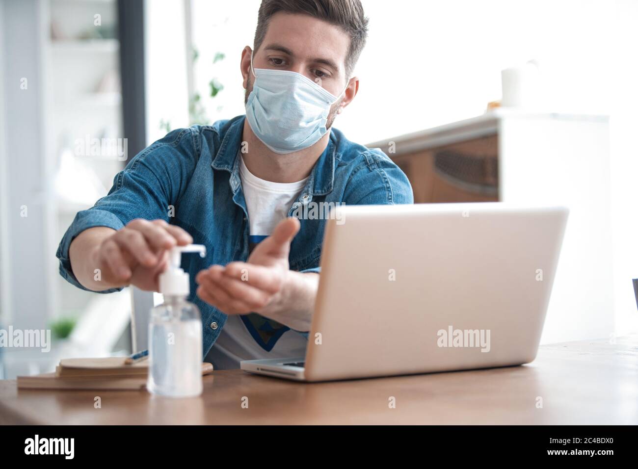Coronavirus. Man working from home wearing protective mask. Cleaning his hands with sanitizer gel Stock Photo