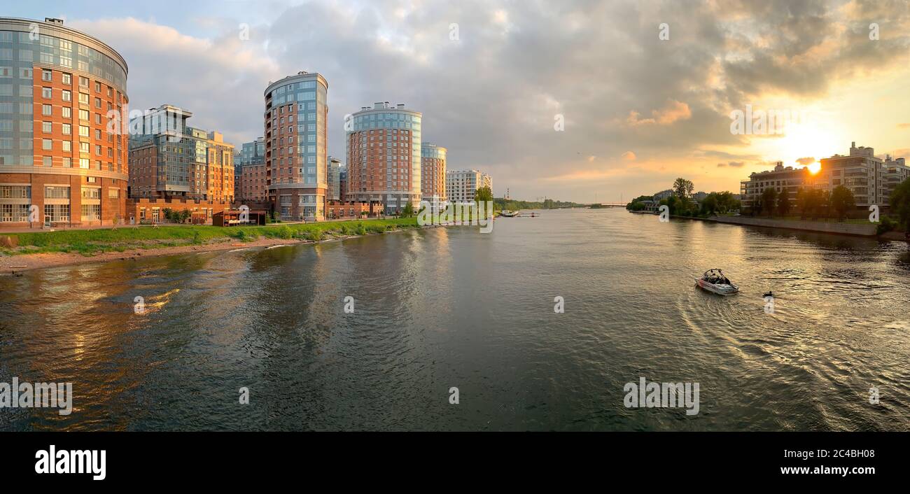 Russia, St.Petersburg, 10 June 2020: The boat with a wakesurfer on a wave goes down the river at sunset, a housing estate on a background, solar Stock Photo