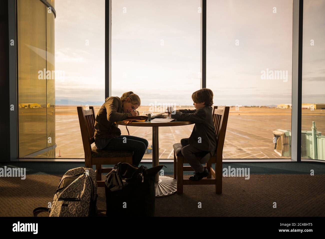A boy and his older sister seated at a table in an airport lounge, writing and drawing. Stock Photo