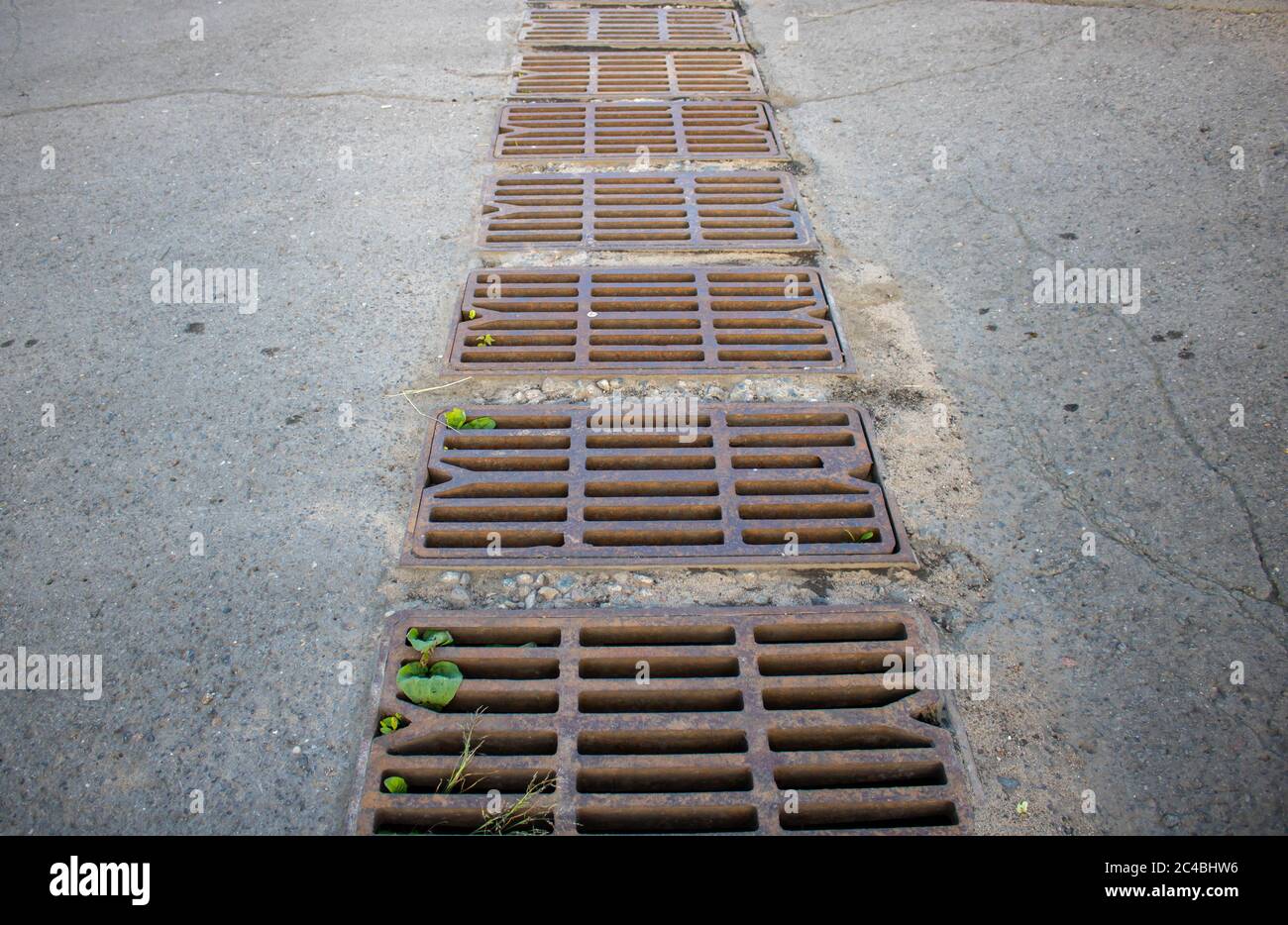 Rusty grating over the drainage channel. Cast-iron radiator grille for the storm sewer on the stone sidewalk. Stock Photo
