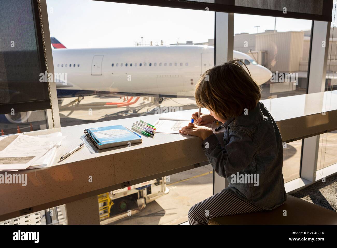 A five year old boy drawing, seated in airport lounge by a window. Stock Photo
