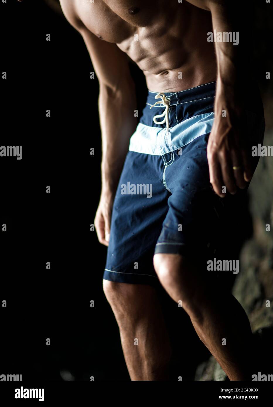 Low section of man with muscular build wearing blue swimming trunks. Stock Photo