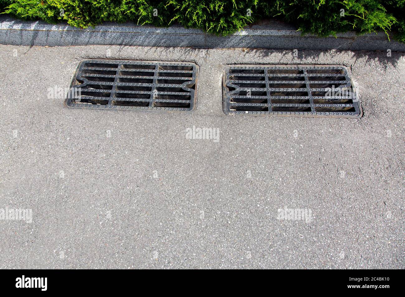 asphalt road with storm drain sewer grate to eliminate water from road surface close-up on a sunny day. Stock Photo