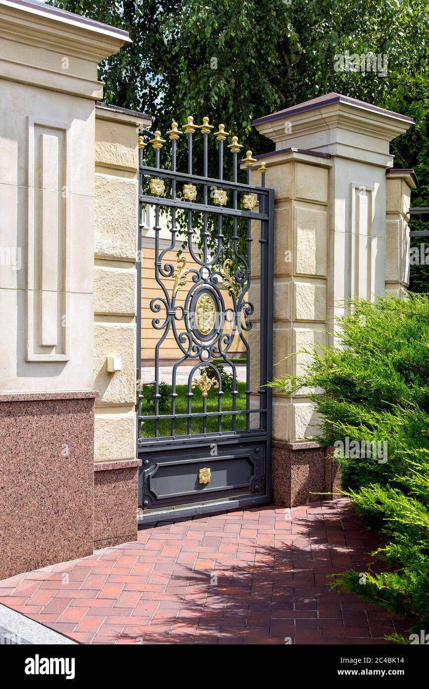 iron wrought iron gates entrance to the territory of the mansion with a  capital stone fence and a garden of trees and a green thuja along the  sidewalk Stock Photo - Alamy