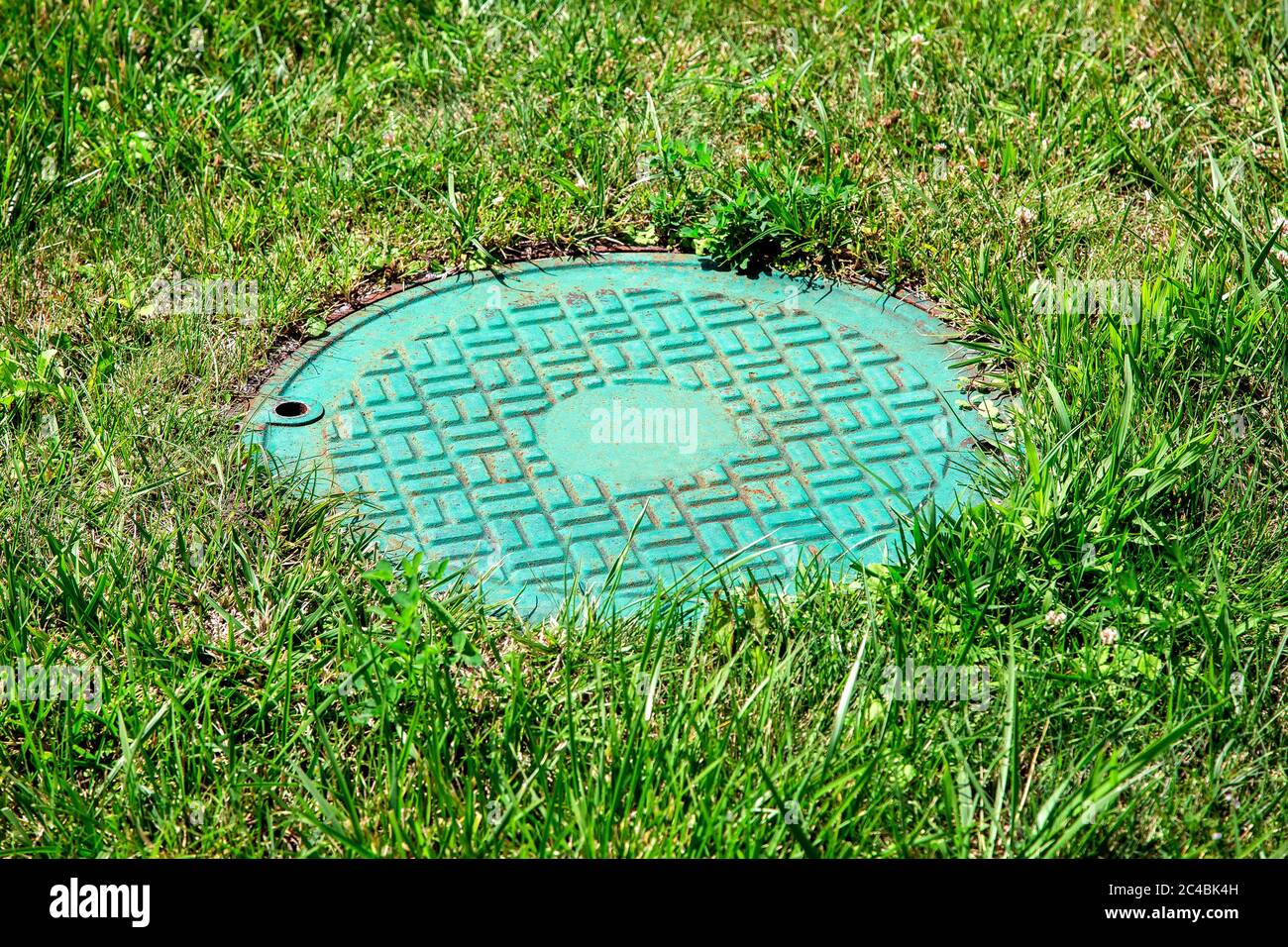 Green iron hatch of a sewer system in a clearing with green grass, close up manhole. Stock Photo