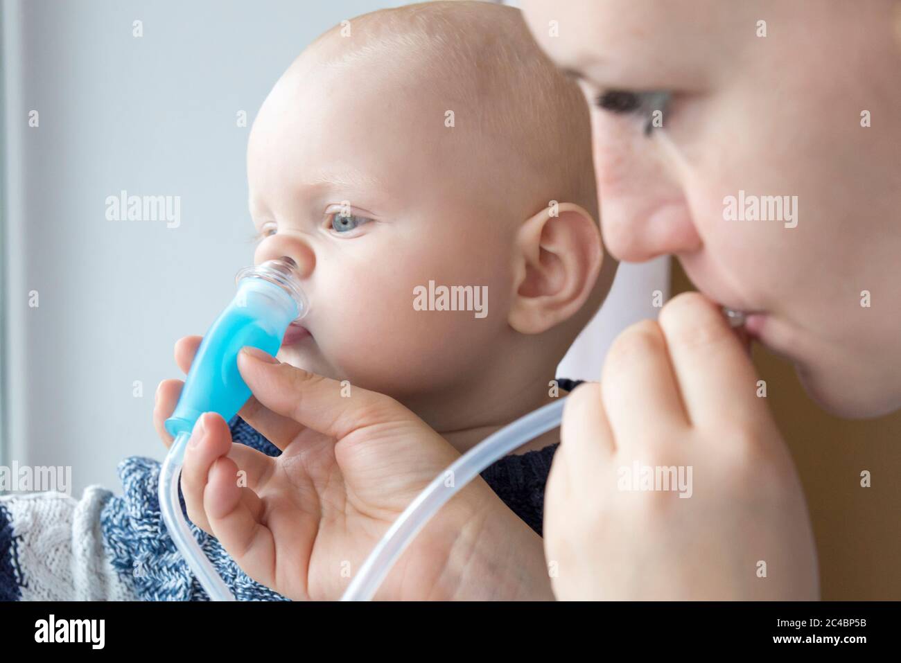 Mom cleans baby's nose from mucus using a nasal aspirator Stock Photo